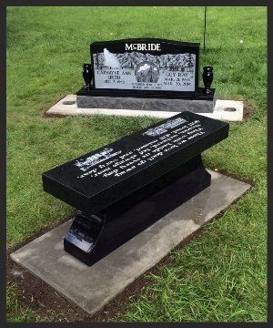 Two black gravestones on a grassy cemetery plot, one upright and one slanted in front.