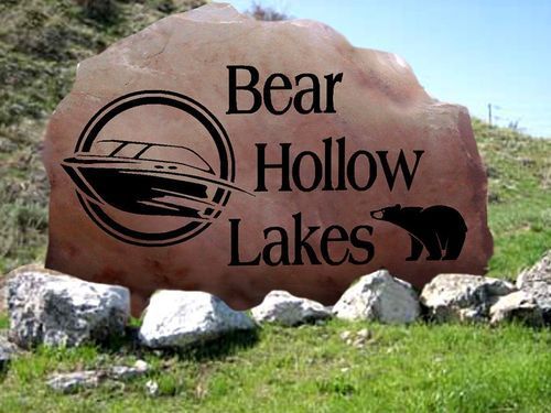 Bear Hollow Lakes sign on a large brown rock with black logo and bear silhouette, outdoors on grass and rocks