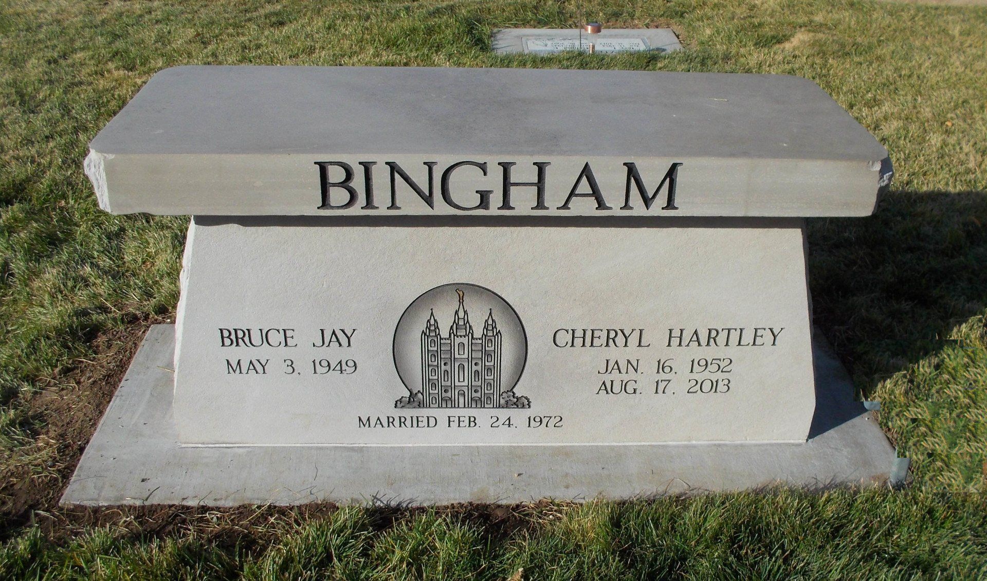Gray memorial bench engraved “BINGHAM” in a grassy outdoor setting