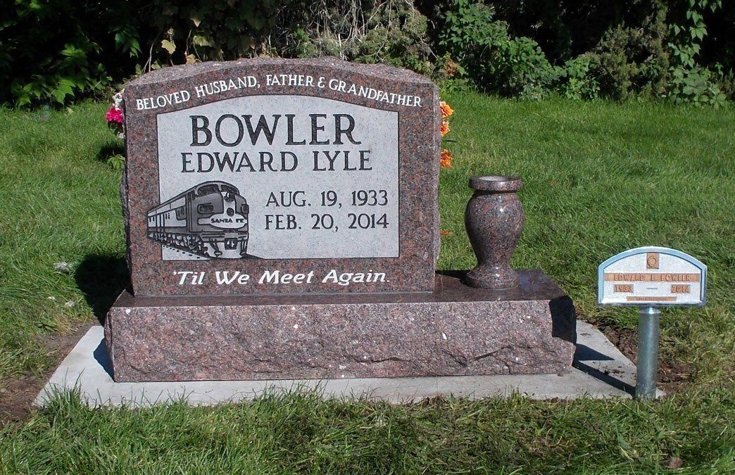Brown granite grave marker in a grassy cemetery, engraved with “BOWLER” and a truck illustration.