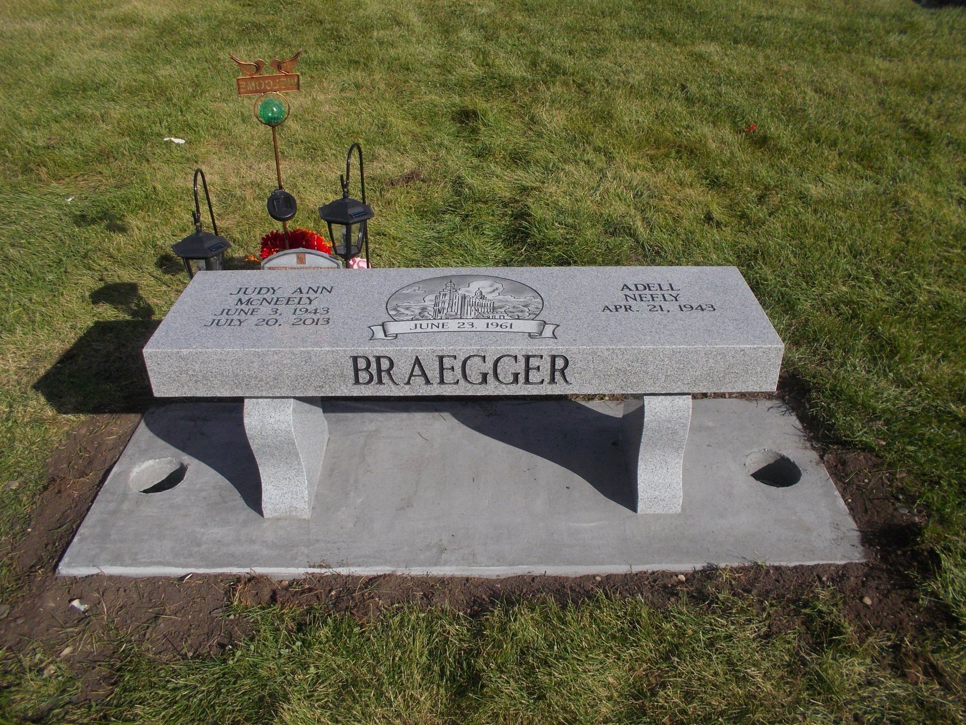Stone memorial marker on a grassy lawn with engraved name and flowers behind it.