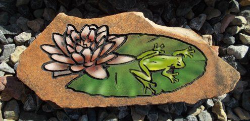 Hand-painted stone with a white flower and green frog on a lily pad among rocks