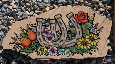 Decorative horseshoe plaque with flowers and roses on a tan background, placed on gravel