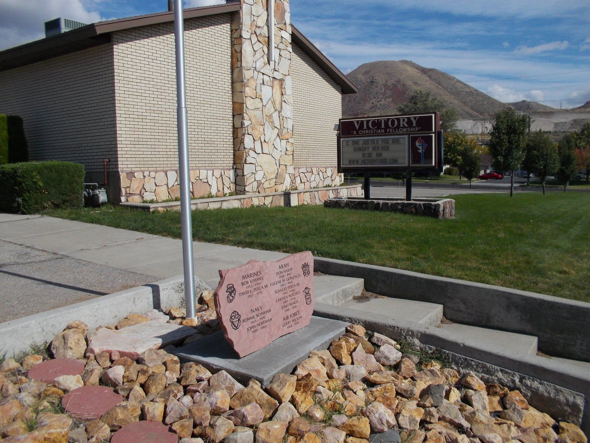 Campus sign near stone building with mountains in the background