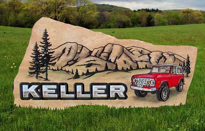Keller sign with mountains and pine trees, featuring a red Jeep on a large tan rock in a grassy field.