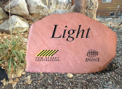 Pink stone sign engraved “Light” in a garden, with Tom Stuart and Anasazi logos.