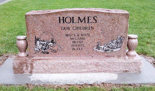 Holmes family memorial stone with engraved text and two small decorative figures in a grassy cemetery.