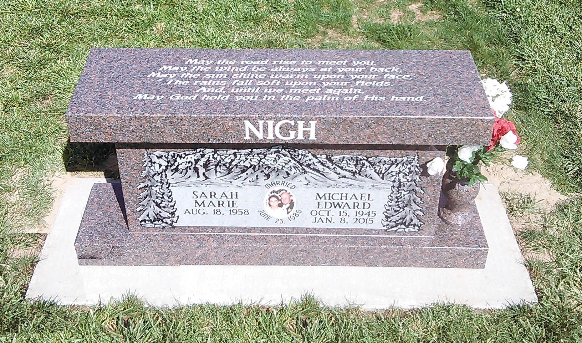 Granite grave marker on a concrete base with flowers beside it, set on a grassy lawn.