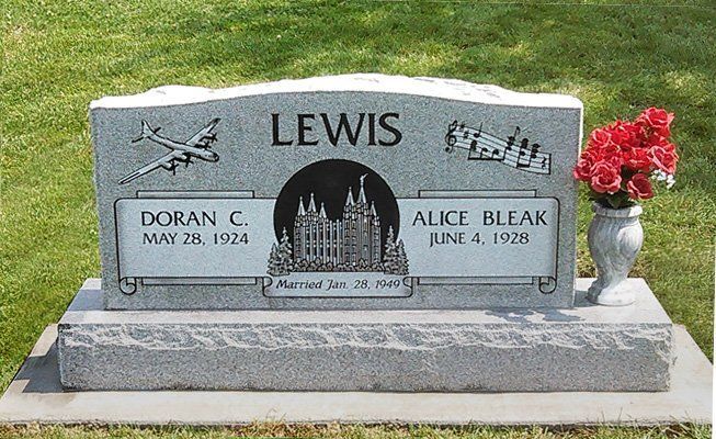 Gray LEWIS family gravestone with engraved cross, two names and dates, beside red flowers on a lawn