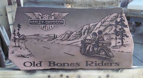 Harley-Davidson “Old Bones Riders” sign with a motorcycle, mountains, trees, and desert scene