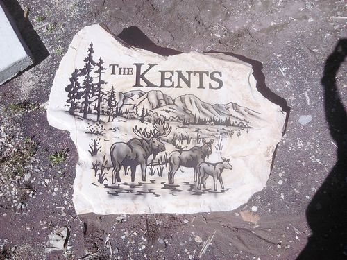 Stone sign with “The Kents” and wildlife scene, including deer and mountains.