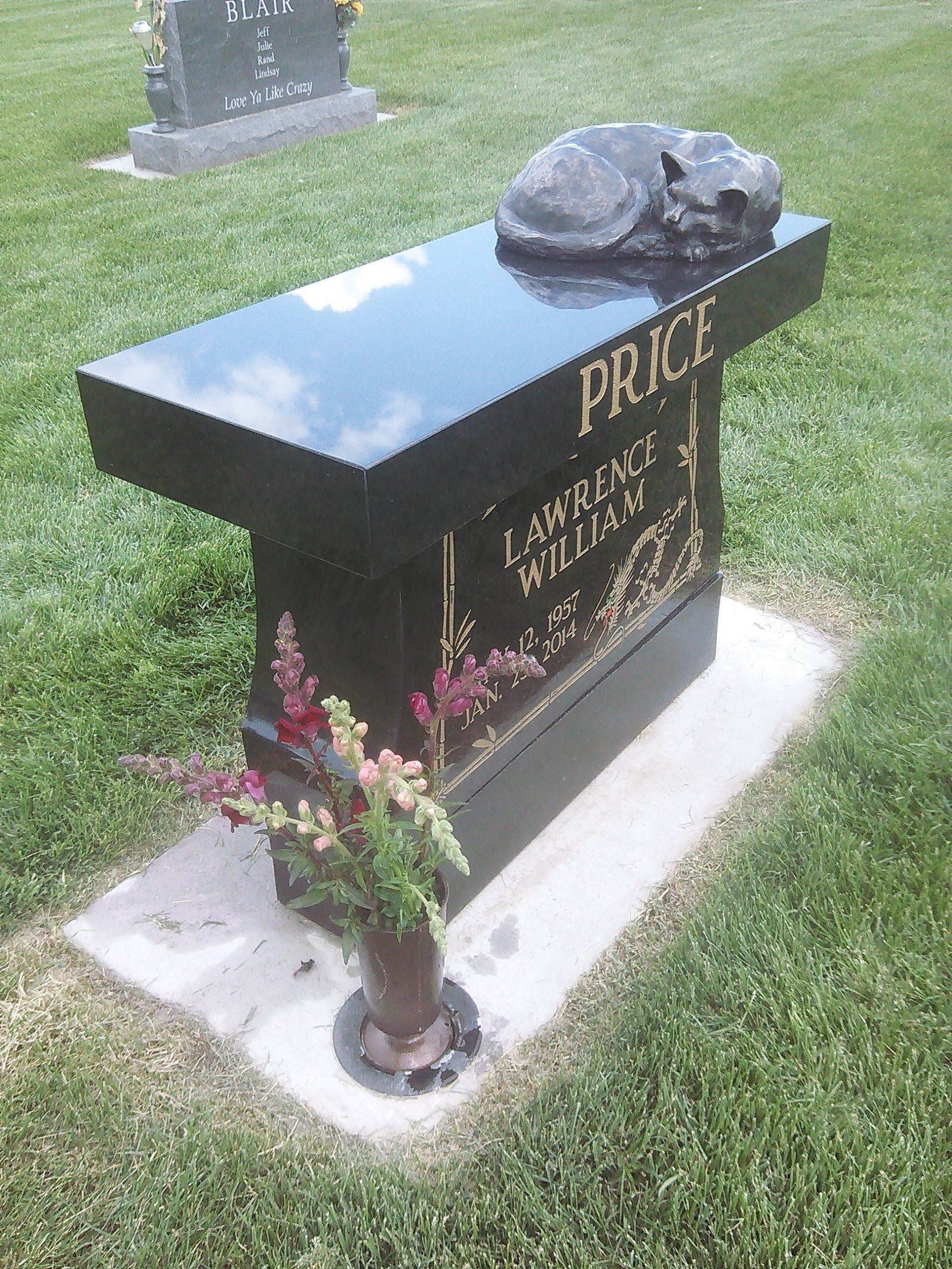 Black polished gravestone with gold lettering and a small flower vase in a grassy cemetery