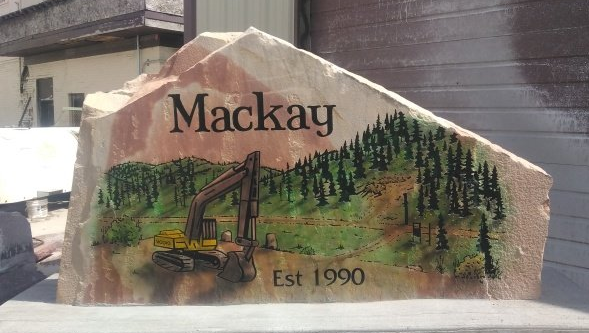 Mackay stone sign with painted logging scene and “Est 1990” text