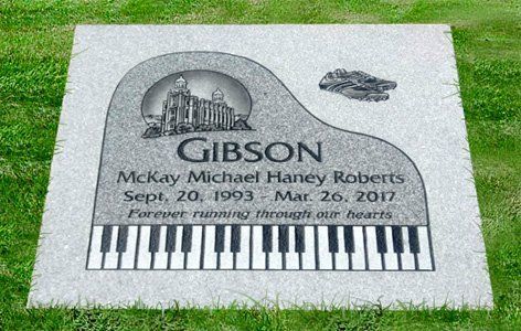 Gravestone with piano keys and “GIBSON” engraved, set in a grassy cemetery.