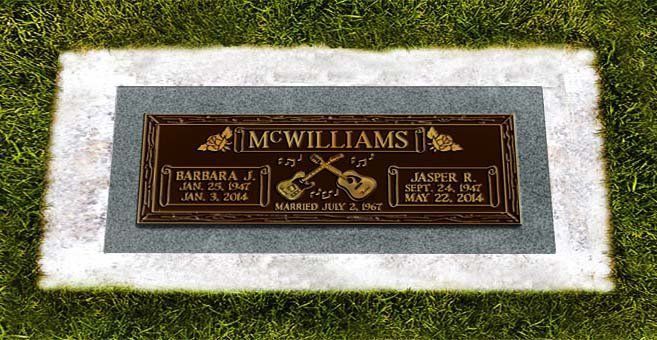 Bronze memorial plaque in a white stone border set in grass, with engraved names and crossed tools.
