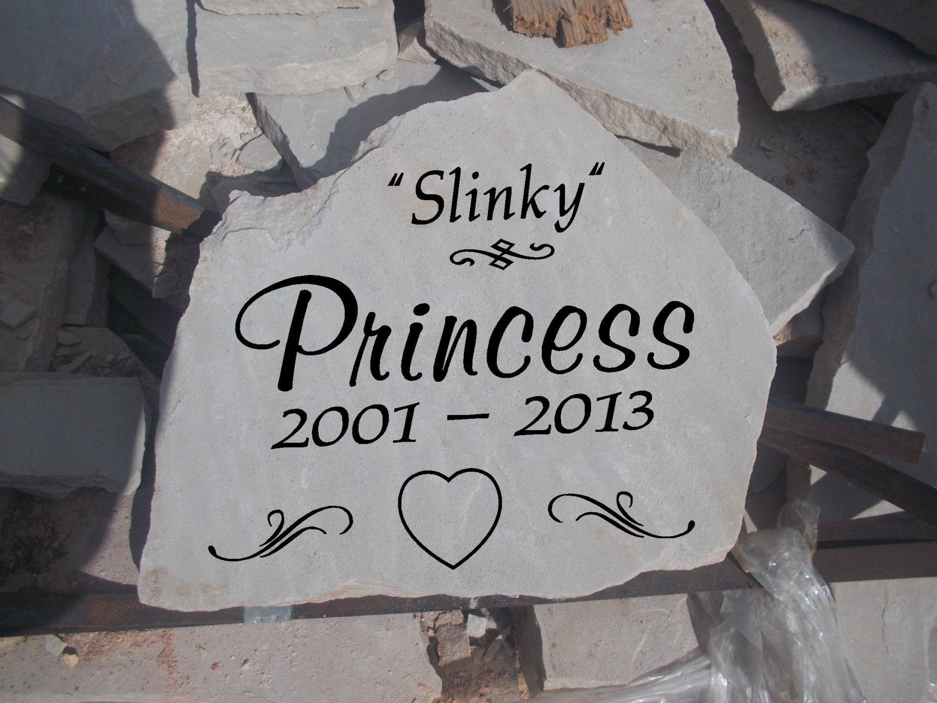 Gravestone for “Slinky Princess” with dates 2001–2013, surrounded by rocks and engraved with a heart.