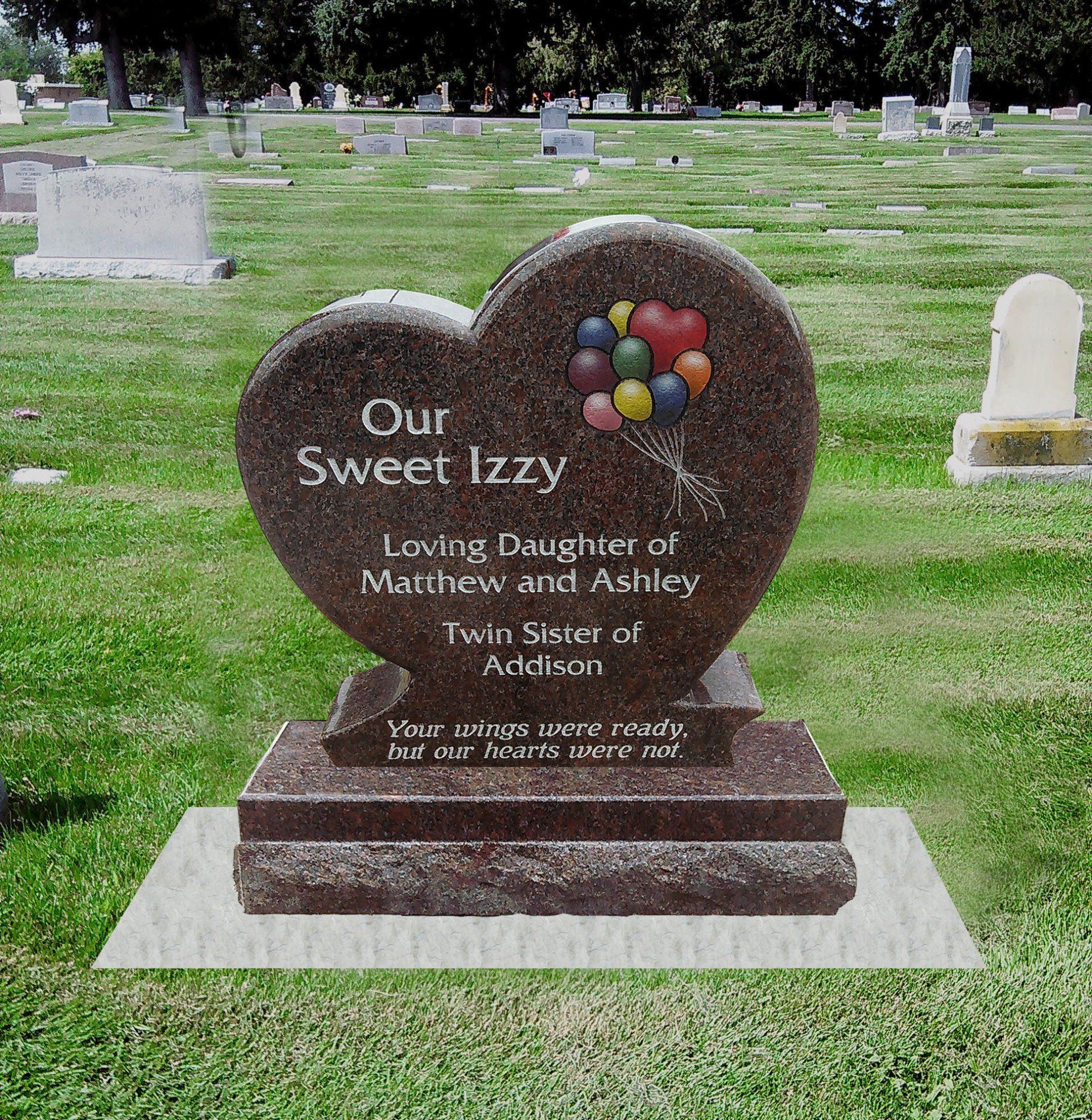 Heart-shaped memorial headstone with colorful balloons in a cemetery.