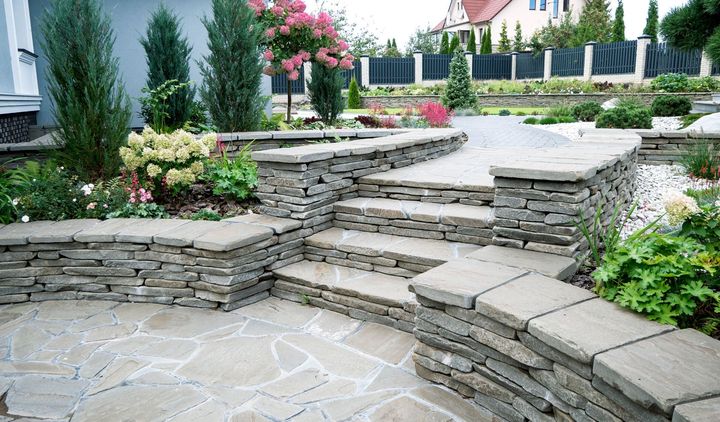 Terraced stone steps and patio in a landscaped garden with flowers, shrubs, and a fenced lawn.