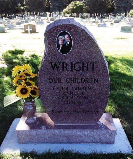 Pink gravestone with oval portrait, “WRIGHT,” and flowers in a cemetery with sunflowers nearby