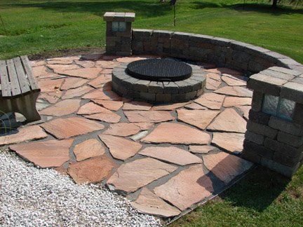 Stone fire pit area with curved brick seating and a flagstone patio in a grassy park.