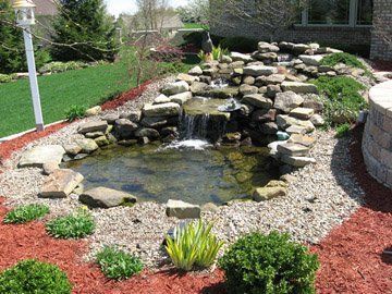 Backyard garden pond with waterfall, rocks, gravel, and red mulch beds