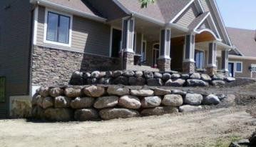 Brick house with a large stacked-rock retaining wall in front and a dirt yard.