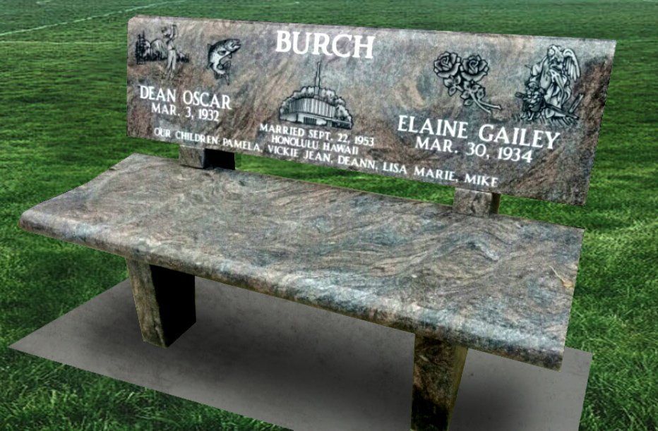 Gray stone memorial bench with engraved family names in a grassy cemetery setting