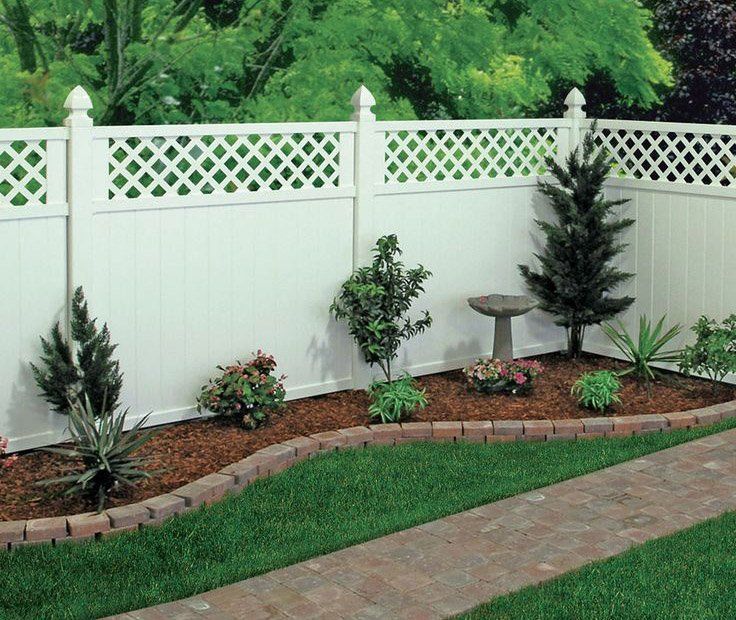 Landscaped backyard corner with white lattice fence, shrubs, mulch bed, birdbath, and green lawn