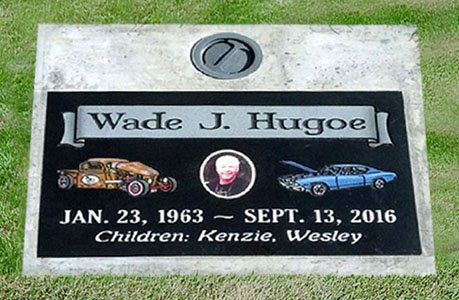 Gravestone for Wade J. Hugoe with dates, small portrait, car and child icons, and “Children: Kenzie, Wesley”