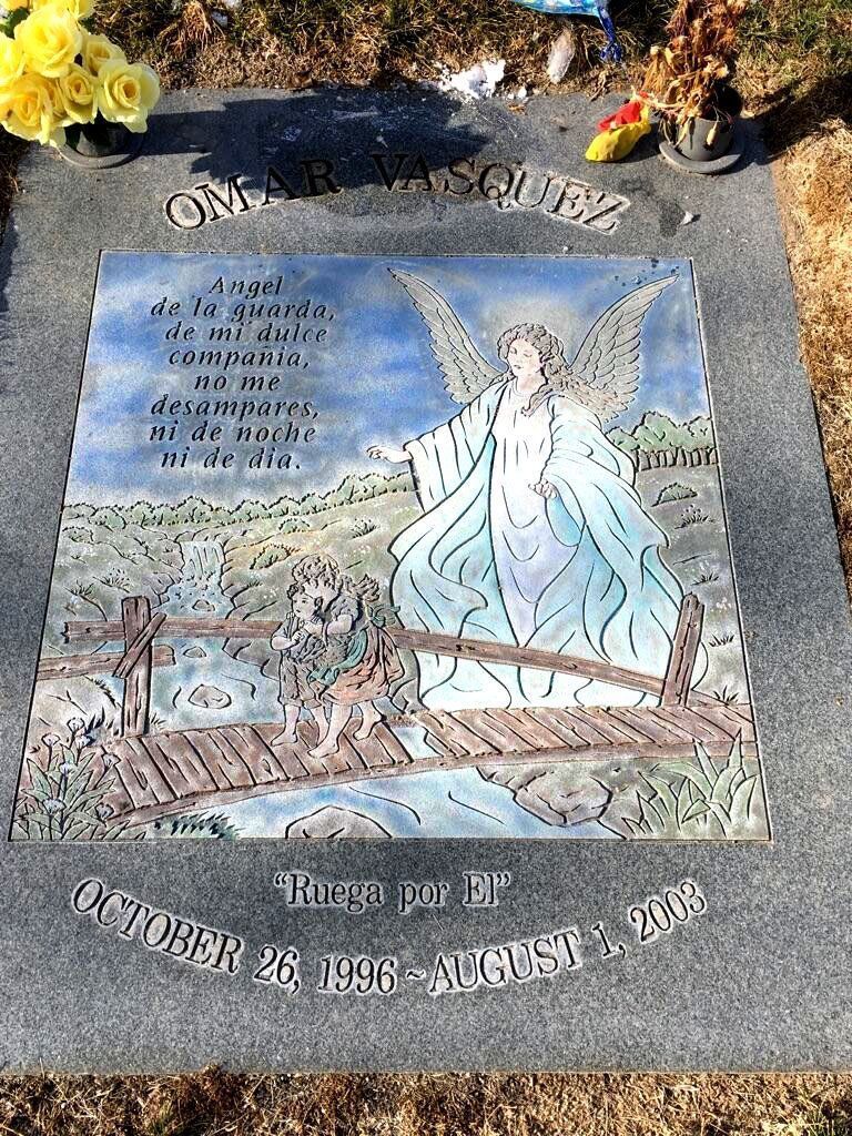 Memorial plaque with an angel illustration and flowers, honoring the dead at a cemetery.