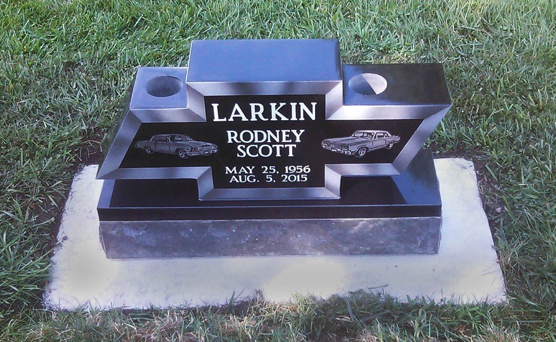 Black gravestone in grass with the names Larkin and Rodney Scott and a small cross emblem