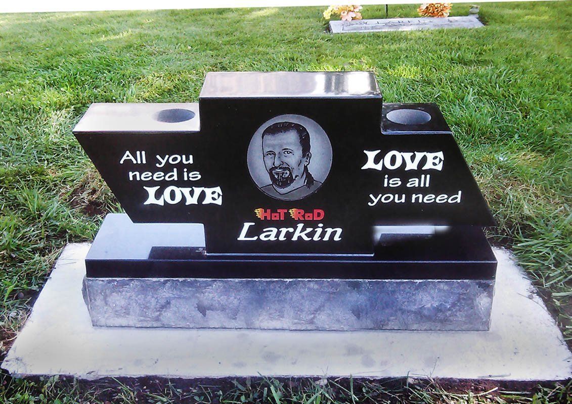 Black grave marker with oval portrait and white lettering: “All you need is LOVE” and “LOVE is all you need.”