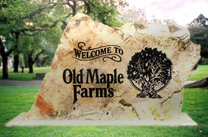Old Maple Farms welcome sign on a stone slab in a grassy park setting