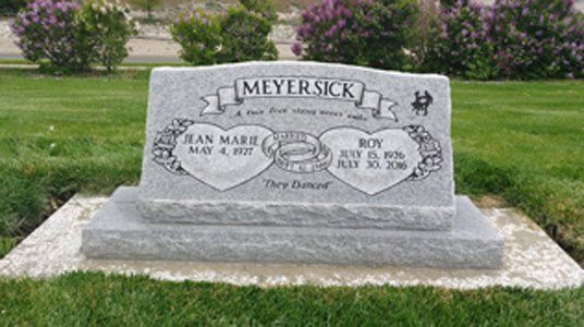 Gray granite Meyersick gravestone in a grassy cemetery with flowers and trees in the background