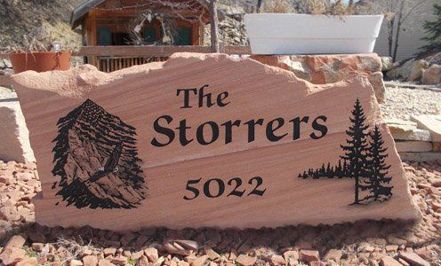 Pink stone sign reading “The Storrers” and “5022” with carved pine trees in a desert setting