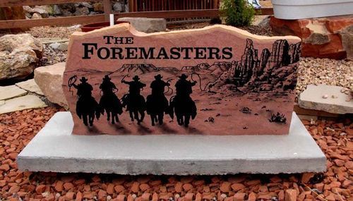 Engraved pink stone sign reading “The Foremasters” with horse silhouettes on a white base in a desert garden