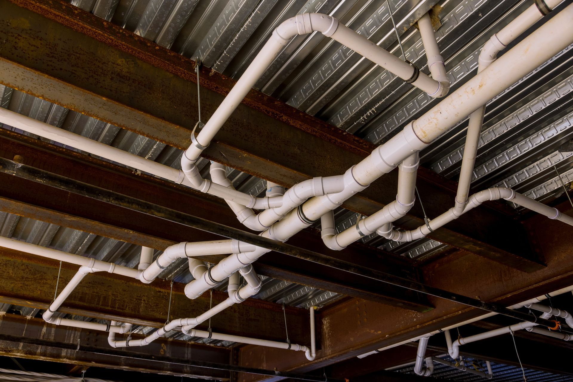 A network of white PVC pipes mounted to a metal corrugated ceiling and steel support beams.