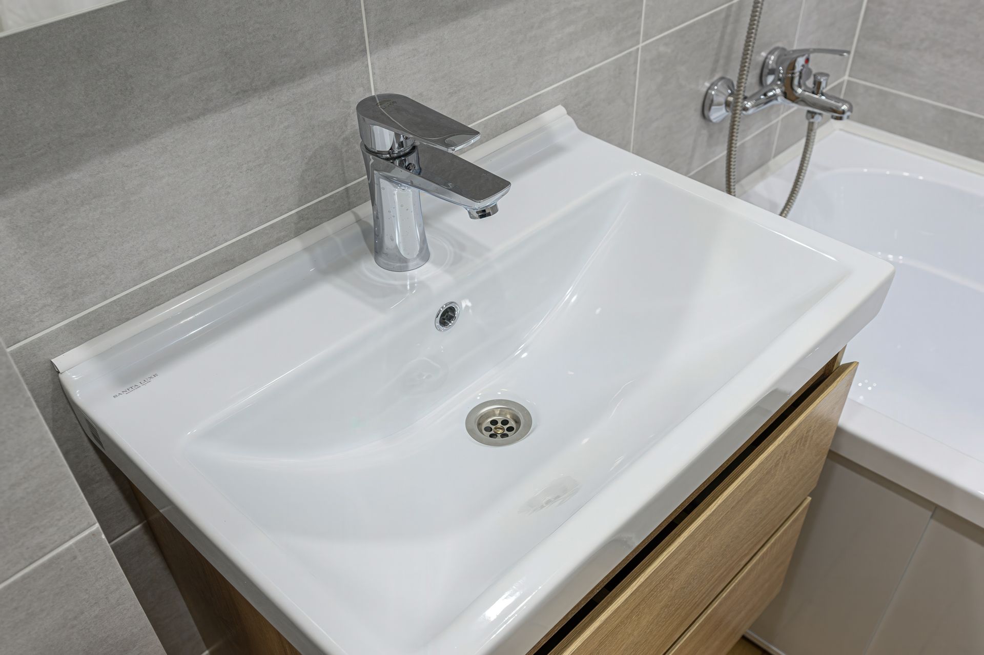 A white ceramic bathroom sink with a chrome faucet, mounted above a wooden cabinet next to a bathtub.