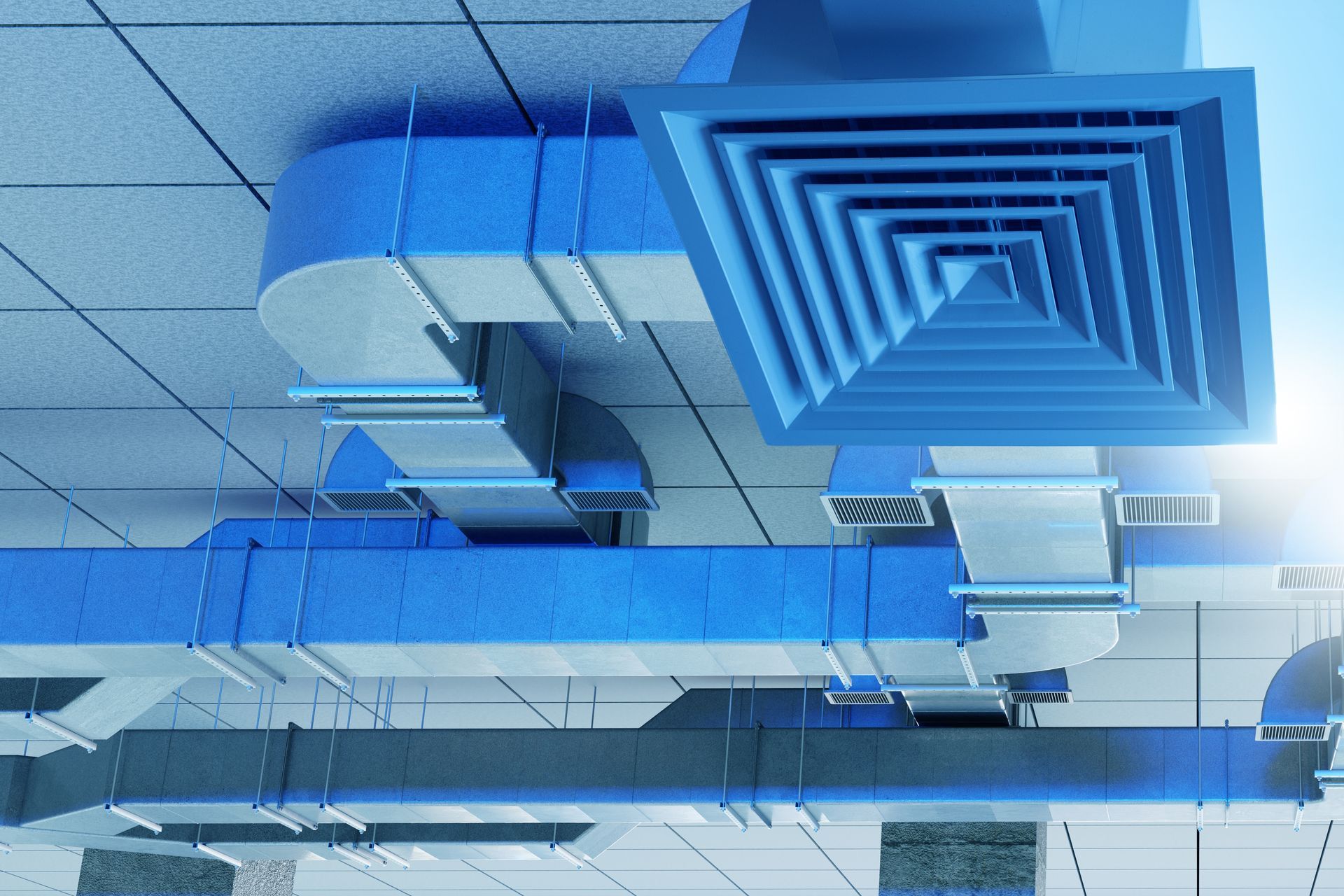 Blue ventilation ducts and a square air diffuser attached to a drop ceiling in an industrial building.