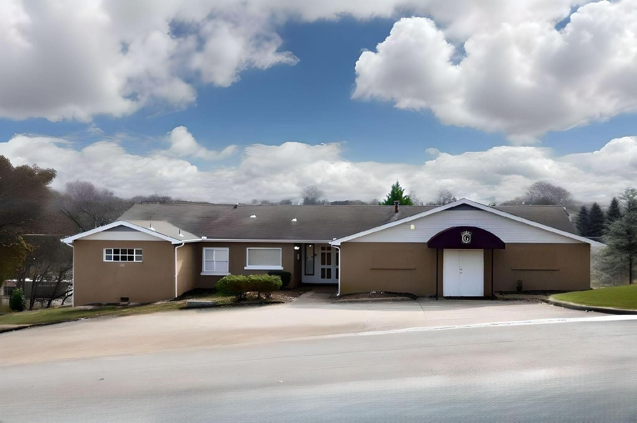 Single-story beige building with a purple entrance under a cloudy sky, seen from a roadside.