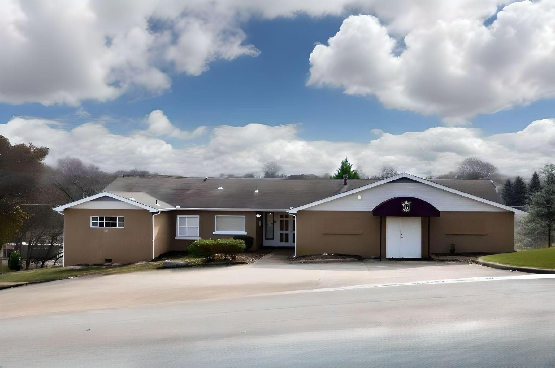 Single-story beige building with a purple entrance under a cloudy sky, seen from a roadside.