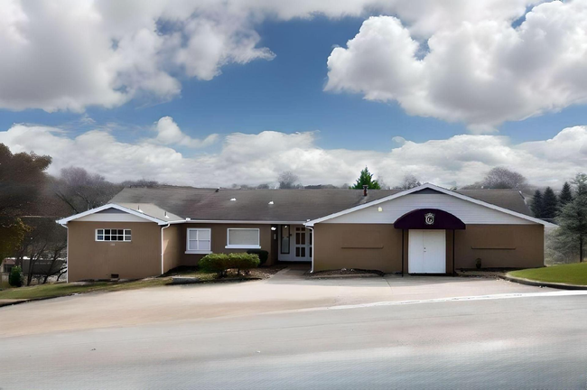 Single-story beige building with a purple entrance under a cloudy sky, seen from a roadside.