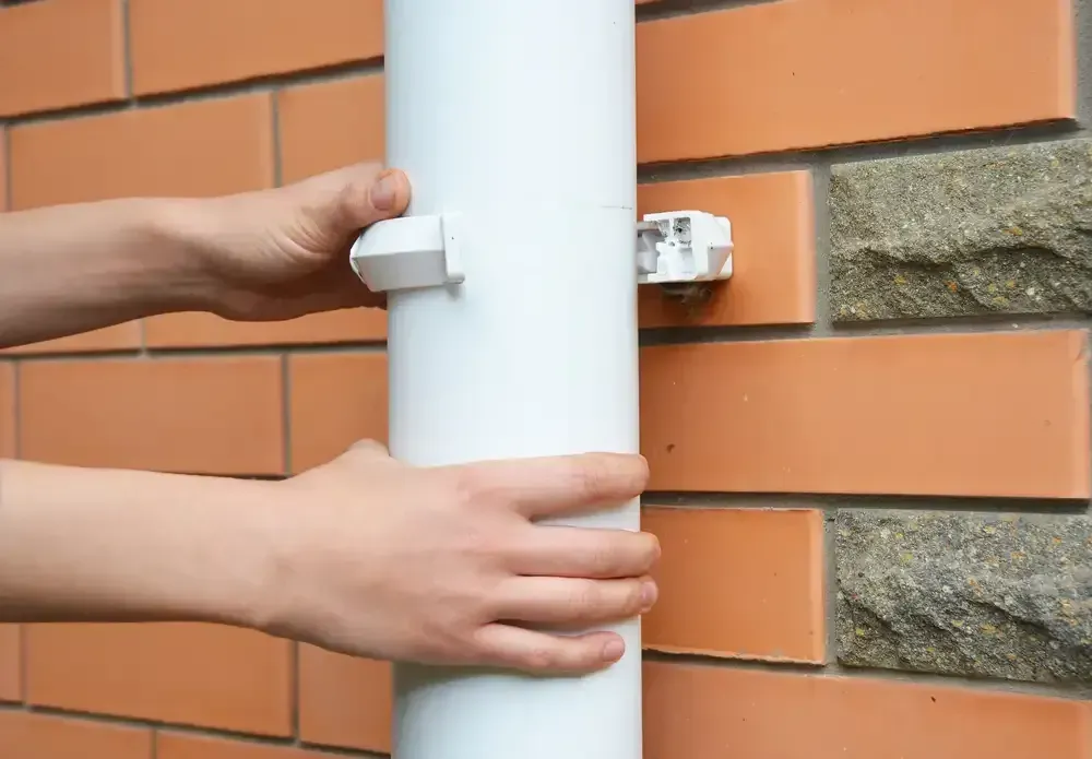 A Person Is Fixing A Gutter On A Brick Wall — Bennett Plumbing In Bulli, NSW