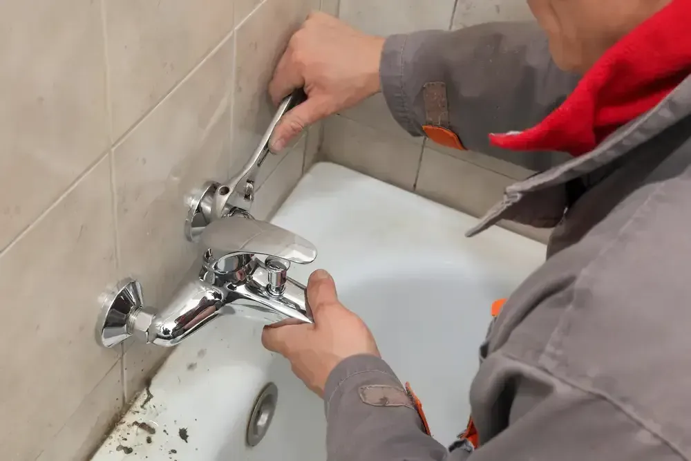 A Man Is Fixing A Bathtub Faucet With A Wrench — Bennett Plumbing In Broughton Village, NSW