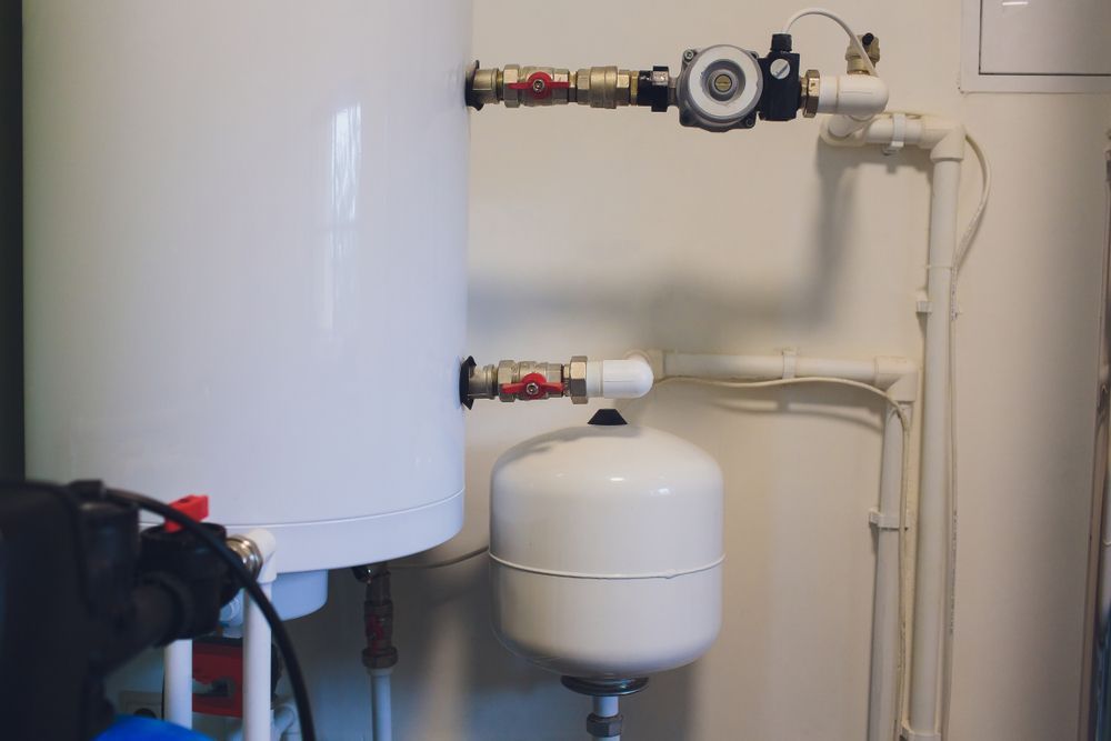 A White Water Heater Is Sitting Next To A White Tank In A Room — Bennett Plumbing In Unanderra, NSW