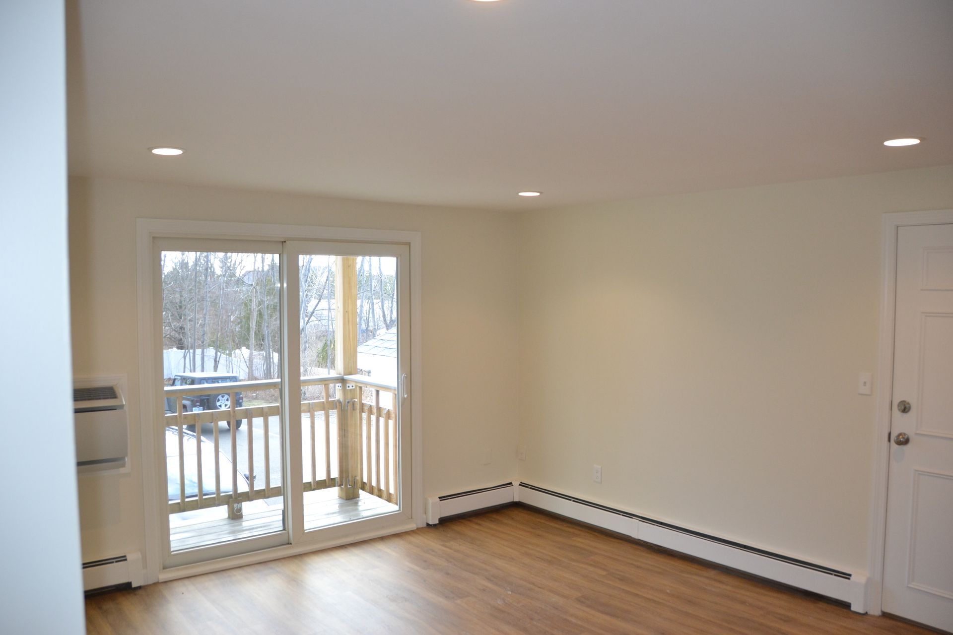 An empty living room with a balcony and sliding glass doors.