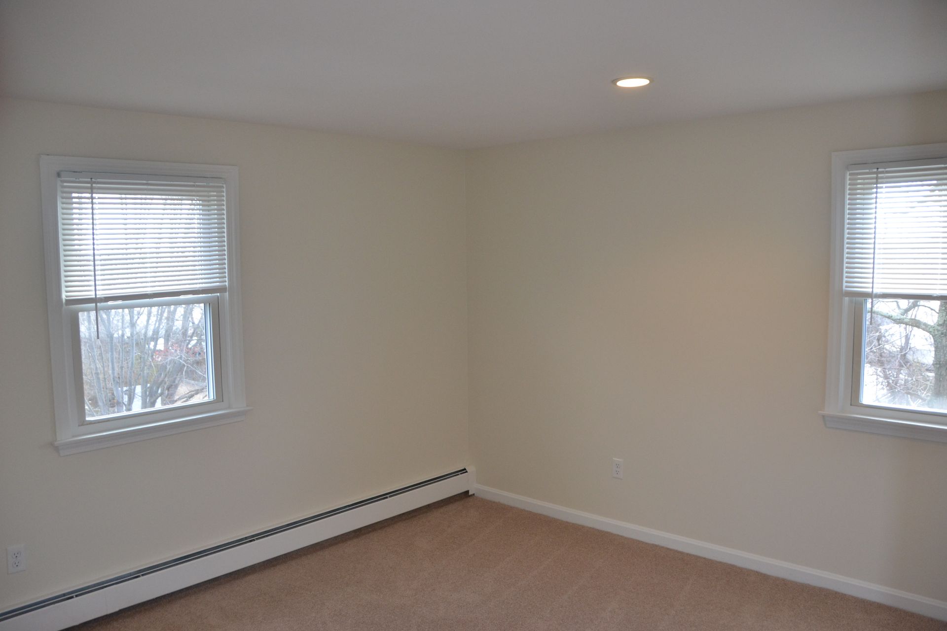 An empty room with two windows and a carpeted floor.