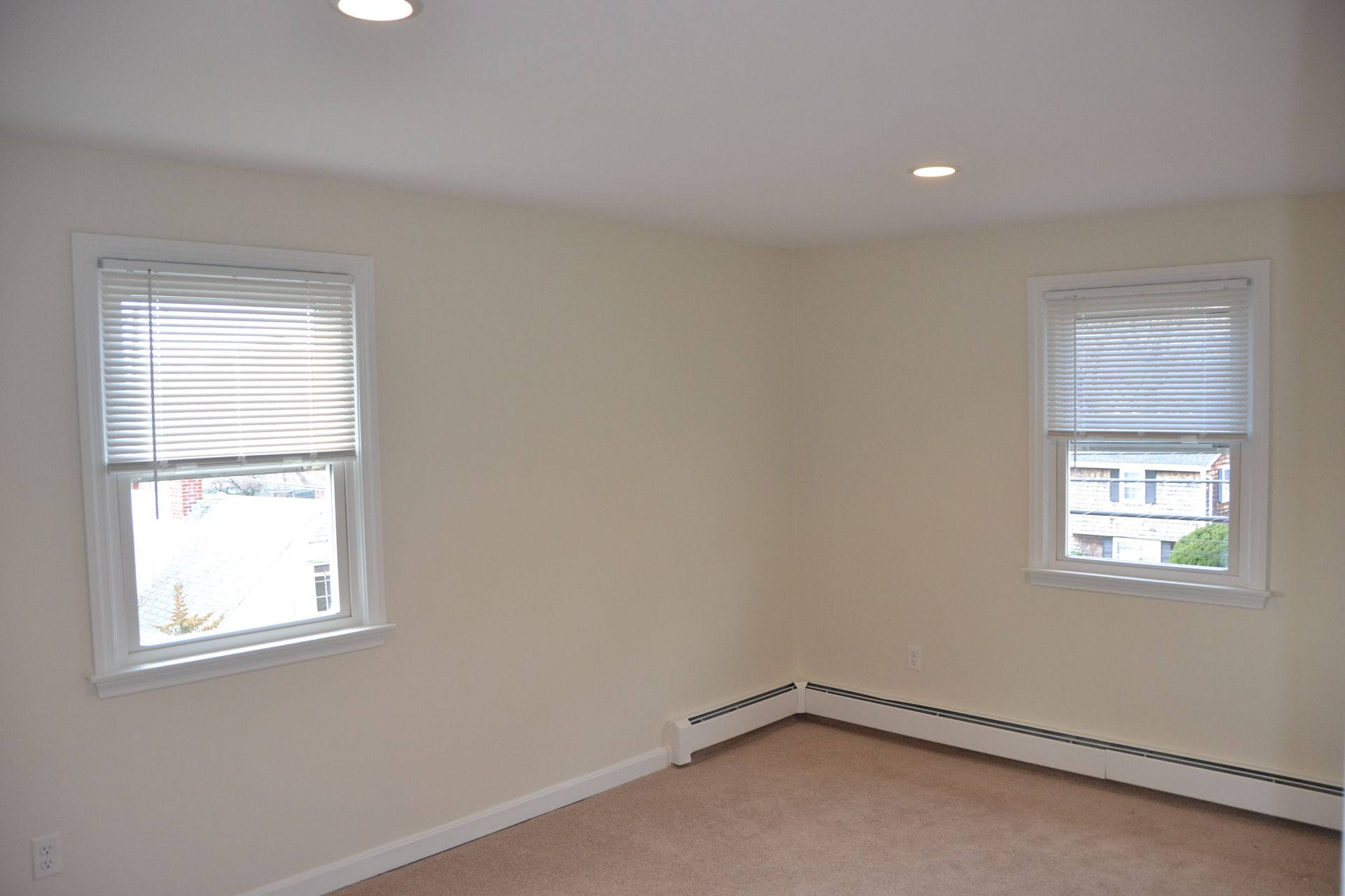 An empty room with two windows and a carpeted floor