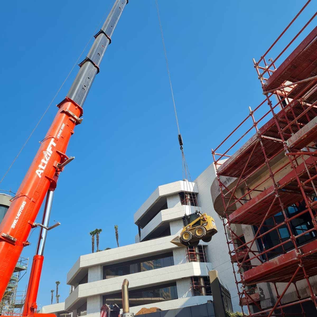 A Large Orange Crane Lifting A Bulldozer — All Lift Cranes In Ulladulla, NSW