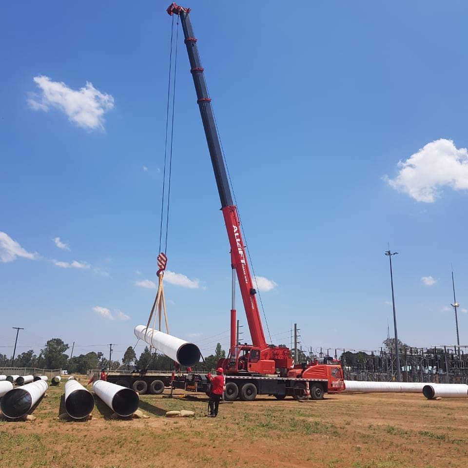 A Red Crane Is Lifting A Large Pipe In A Field — All Lift Cranes In Batemans Bay, NSW